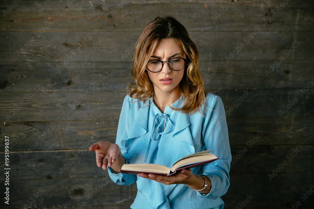 Beautiful business woman looks confused while reading a book. Dressed in blouse, in eyeglasses.
