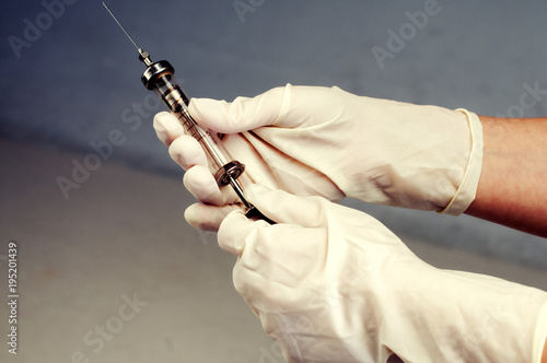 Hand squeezing an old glass syringe with a sharp needle photo