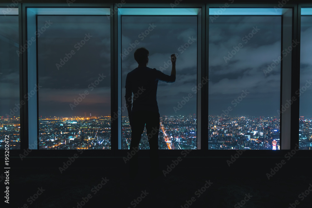 Fototapeta premium Man writing on large windows high above a sprawling city at night