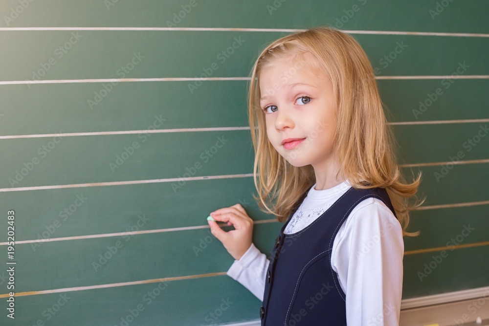 First grade pupil a girl writing on green blackboard at school lesson First grade pupil a girl writing on green blackboard at school lesson