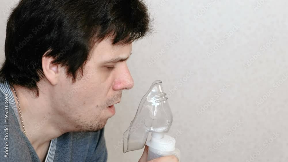 Use nebulizer and inhaler for the treatment. Young man inhaling through inhaler mask and coughs. Side view.