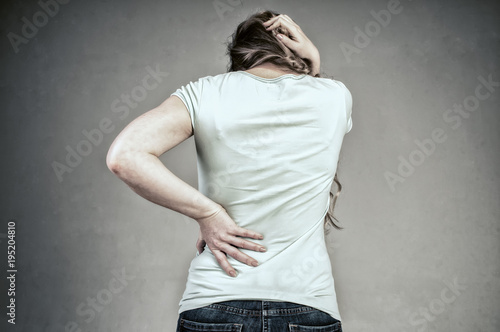 A young girl from the back with a strong headache and back pain. Convulsive spasm and headaches concept. Woman with back pain holding her aching back - body pain