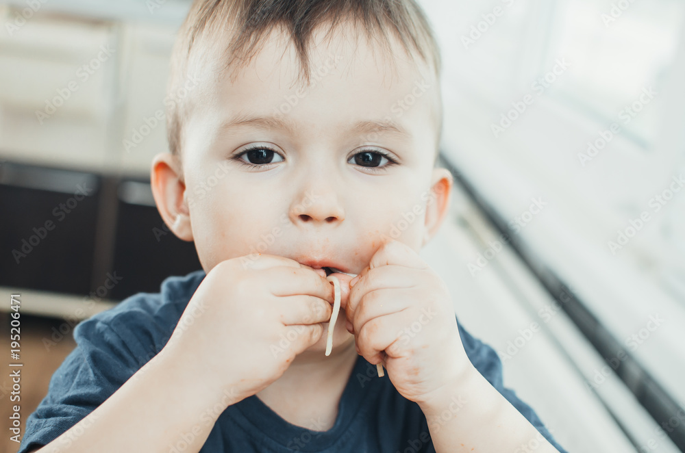 A beautiful cheerful child eats pasta with his hands, spaghetti all dirty