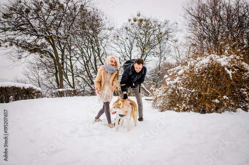 A lovely couple plays with her dog in a snowy park
