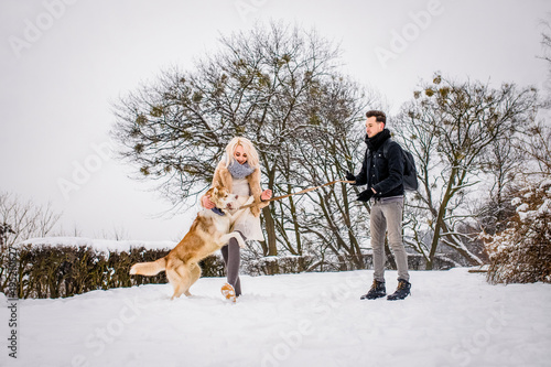 Smiling couple plays with her dog in a snowy park photo