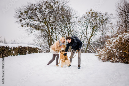 A lovely couple plays with her dog in a snowy park