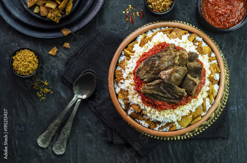 Arabic cuisine, Egyptian oriental Fettah with white rice and crispy bread topped with seasoned garlic red sauce,crispy fried garlic and veal chunks on rustic dark background.Top view,close-up