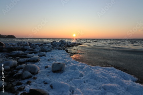 malerische Lichtstimmung bei Sonnenaufgang an einer Buhne mit vereisten Steinen im Winter am Meer