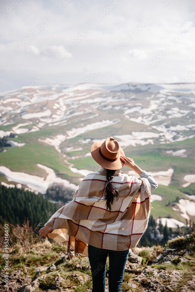 Traveling woman standing in the wild in front of an amazing view. Hat, poncho. Winter is coming, first snow. Passion for travel and boho style