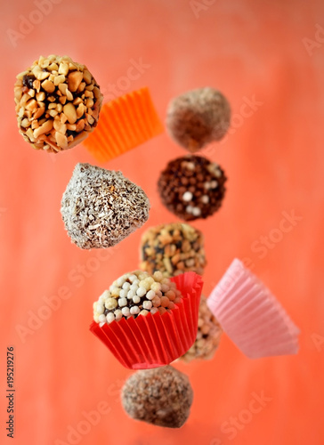 Photography Flying sweets with different sprinkles and paper cups on colourful orange backgr