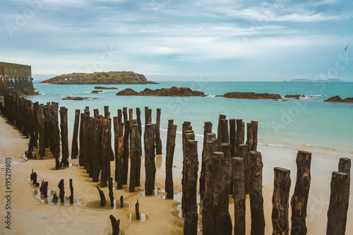 Wooden poles along the coastline and tidal island Grand Be with remains of ancient fort and tomb of French writer Chateaubriand in background near Saint-Malo, Brittany, France