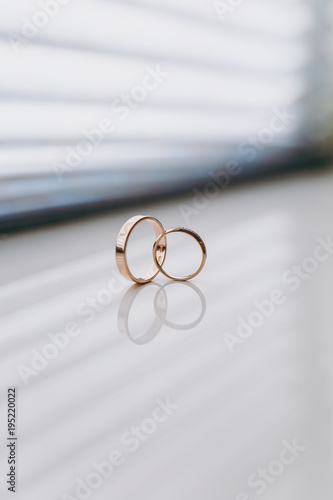 Close up Two beautiful stylish gold wedding rings of the bride and groom intersect on a white gloss windowsill background. Wedding accessories, jewelry
