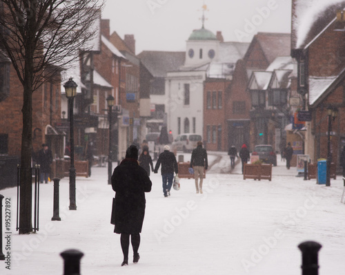 people walking through typical English street during blizzard with virgin snow on ground