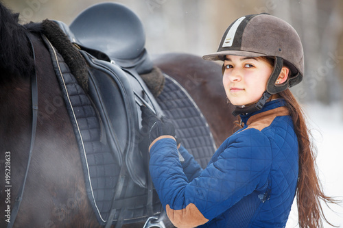 Photography Young girl adjusting stirrups and saddle before riding her bay horse