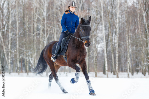 Young rider girl on bay horse galloping in winter. Equestrian winter activity background