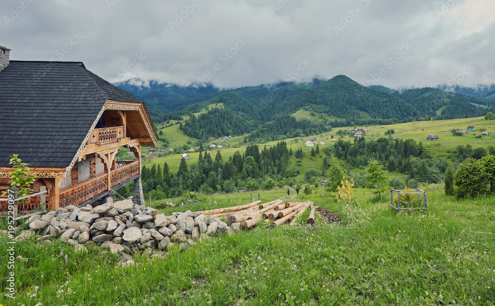 A wooden house on a green meadow in mountains. A house near old forest. A wooden house on a green meadow in mountains. A house near old forest.