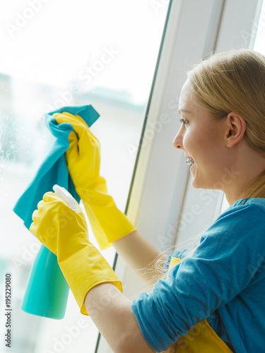 Girl cleaning window at home using detergent rag