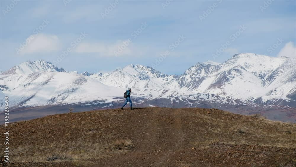 Hiker woman with backpack hiking on top of a mountain. Female tourist using smart phone for taking photo or video. Snowy mountains around Hiker woman with backpack hiking on top of a mountain. Female tourist using smart phone for taking photo or video. Snowy mountains around