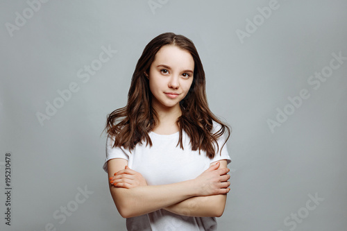 Portrait of a pretty smiling woman brunette in a white t-shirt posing isolated on a white background. the girl smiling into camera rejoicing her success, standing with folded arms.