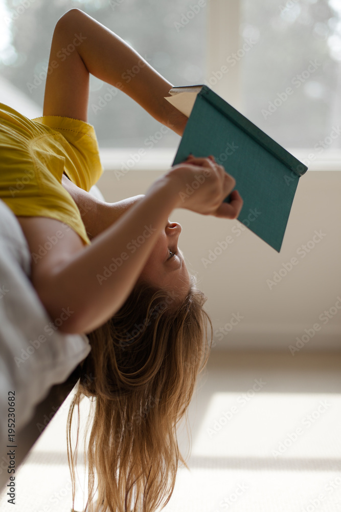 Girl hanging upside down off edge of bed while reading a book Stock