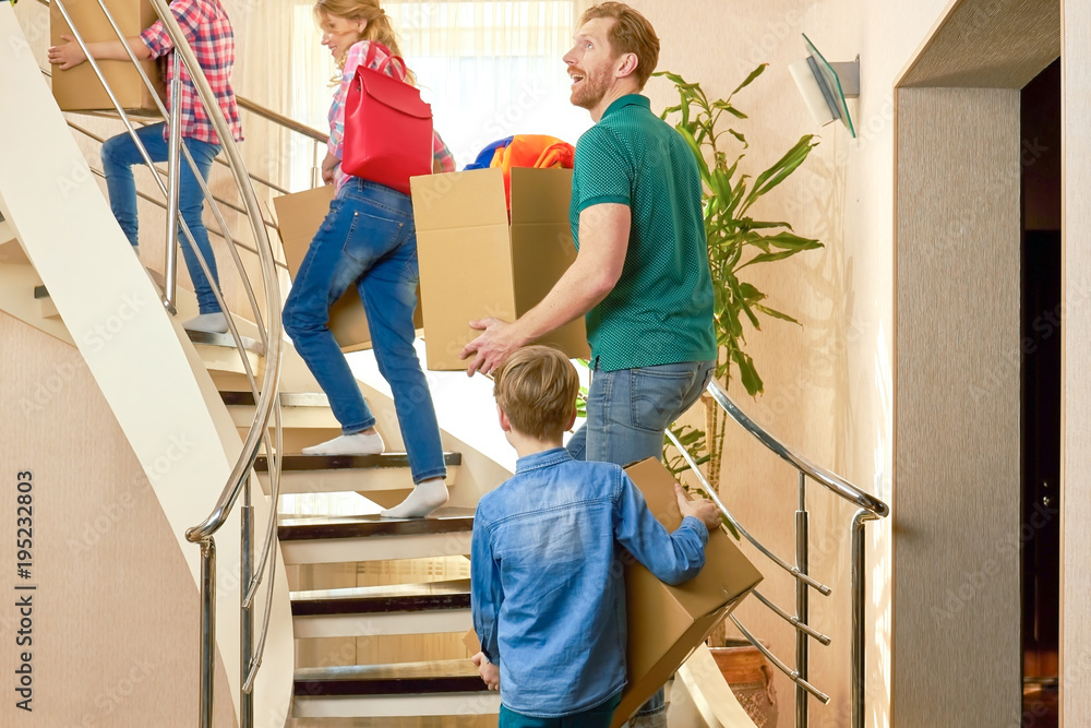 Family carrying boxes upstairs. Group of people indoors. Moving to a