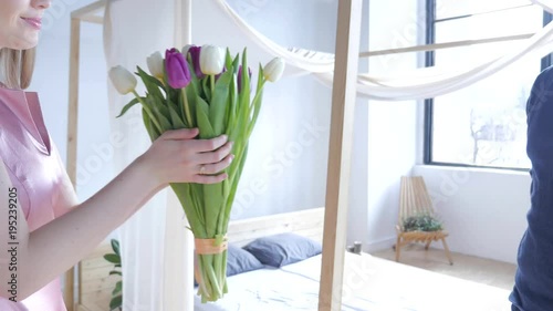 Young man is presenting flowers to his beloved. Woman receiving a bunch of tulips on a date. Man and woman hand holding flowers. Beautiful romantic couple in love. Man hands gives his wife a bouquet. 