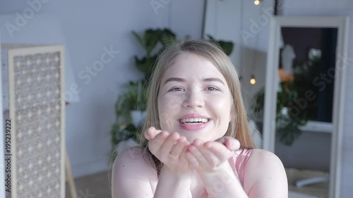 Woman blowing sparkles. Close up portrait of attractive young woman blowing glitters. Caucasian Female model having fun over room background. Girl blowing glitter, celebration concept. Girl smiling. 