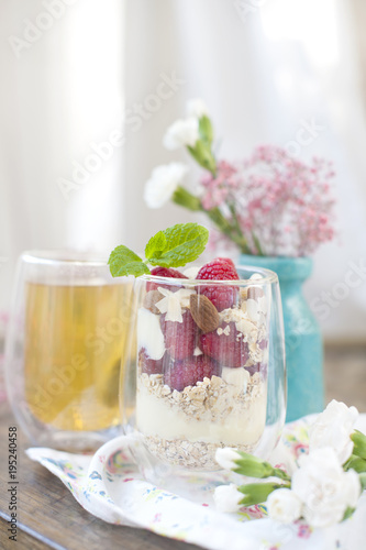 Useful breakfast of muesli and yogurt with berries in a glass. Tea in a glass. A bouquet of flowers in a blue vase. Spring breakfast at the window of the house.