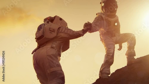 Two Astronauts Climbing Mountain Hill Helping Each Other, Reaching the Top. Helping Hand. Overcoming Difficulties. photo