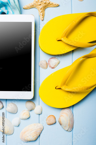 Summer women's accessories: sunglasses, yellow step-ins, dress, tablet, camera, on blue wood background. photo