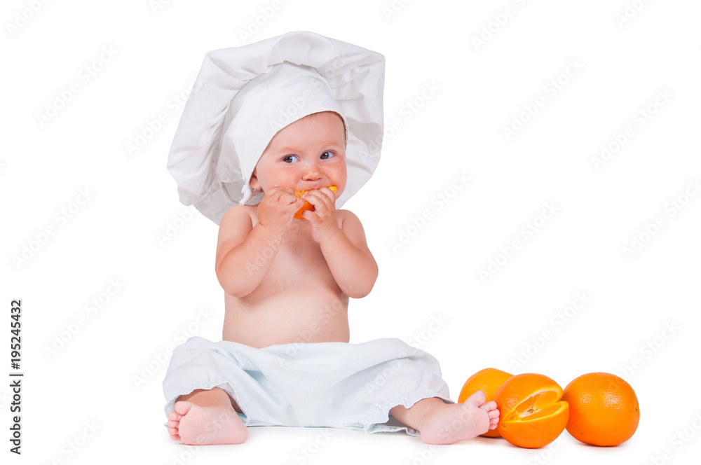 A small child eats an orange slice in a chef suit on a white background. A small child eats an orange slice in a chef suit on a white background.