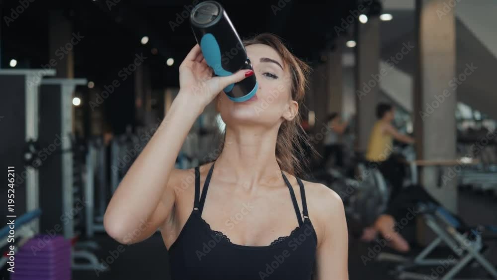Young athletic woman drinking water in gym after hard workout . Young athletic woman drinking water in gym after hard workout .