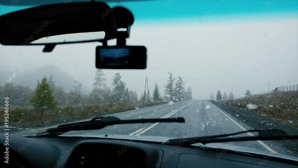 Driving by car in real winter conditions, view from inside out on snow covered road. First snow at autumn day. Car and falling snow in winter on forest road Driving by car in real winter conditions, view from inside out on snow covered road. First snow at autumn day. Car and falling snow in winter on forest road