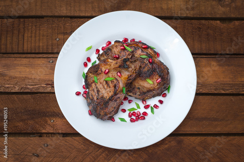 Steak on ribs, cooked on a grill with pomegranate on a white plate. Wooden rustic background. Top view