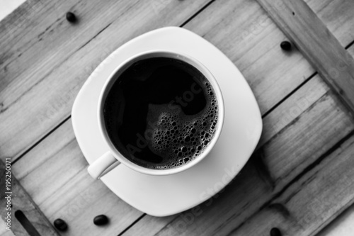 Single white cup with black coffee on wooden table with few beans black and white photography