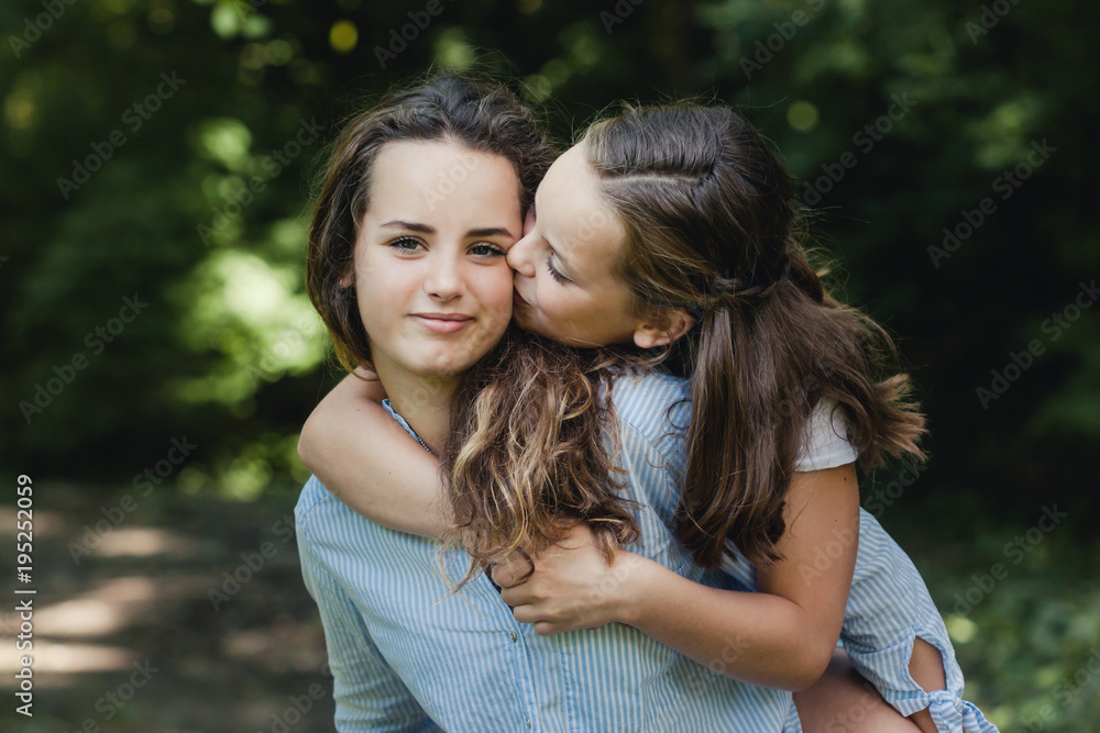Sweet portrait of little girl giving her big sister a kiss Sweet portrait of little girl giving her big sister a kiss