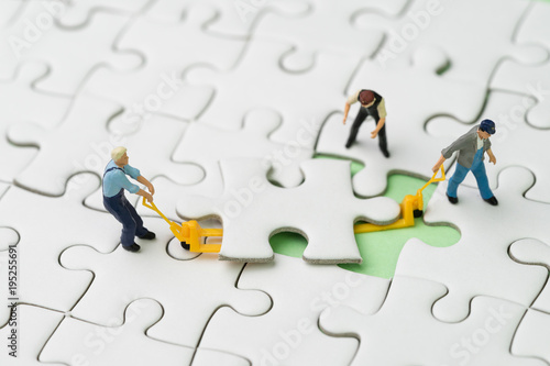 Teamwork, fulfill the missing piece for business success strategy concept, miniature workers team help using the forklift to complete the missing white jigsaw puzzle piece on pastel green background
