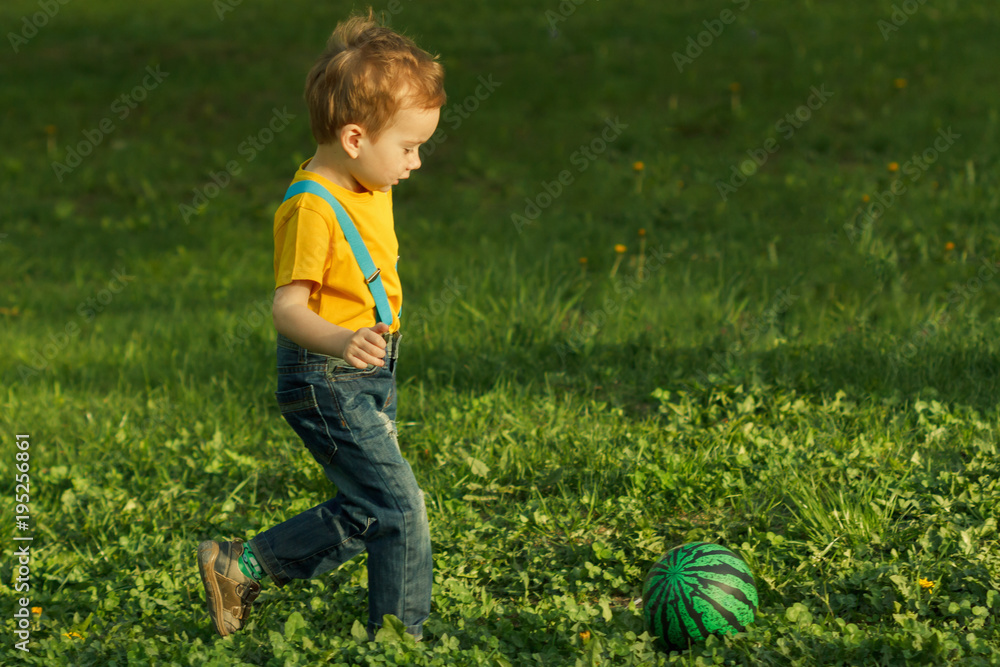 Cute positive kid, playing happily with ball on green meadow Cute positive kid, playing happily with ball on green meadow