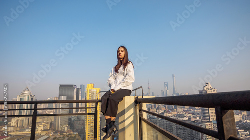 Beautiful young brunette woman sit on top of mansion roof with blur Shanghai Bund landmark buildings background. Emotions, people, beauty and lifestyle concept.