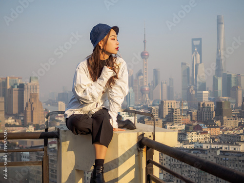 Photography Beautiful young brunette woman sit on top of mansion roof with blur Shanghai Bund landmark buildings background