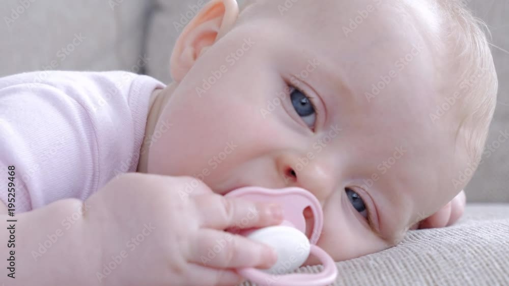 Little small girl playing with pacifier while lying on sofa Little small girl playing with pacifier while lying on sofa