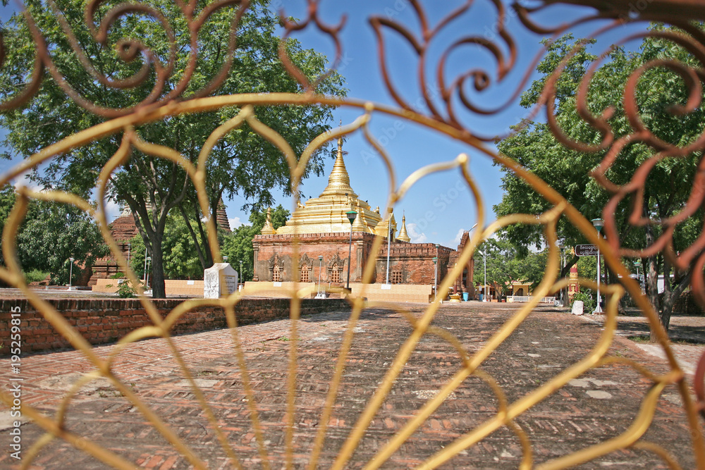 An ornate metal gate leads towards a shining golden topped building in Bagan, Burma