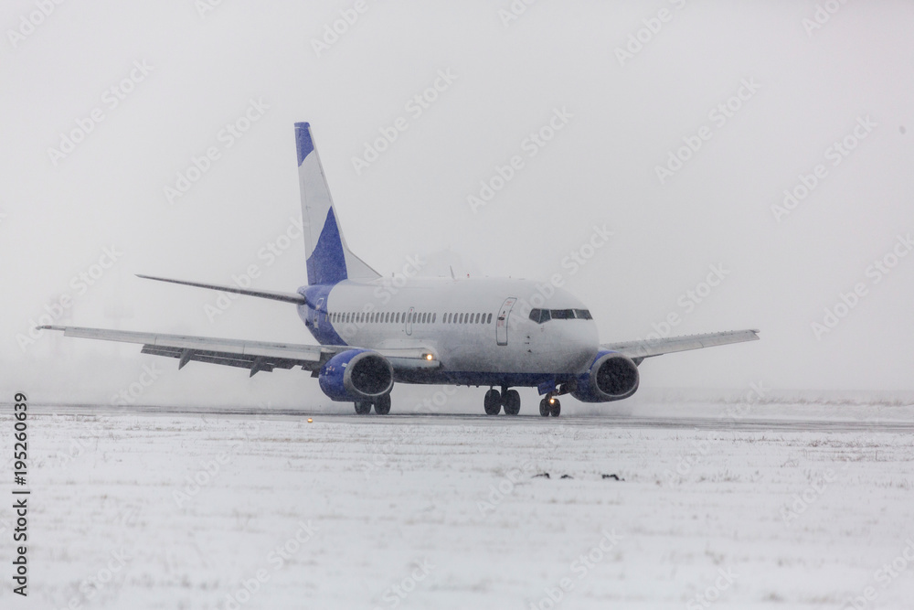 Obraz premium Airliner on runway in blizzard. Aircraft during taxiing at heavy snow. Passenger plane in snow at airport. Modern twin-engine passenger airplane taxiing for take off at airport during snow blizzard