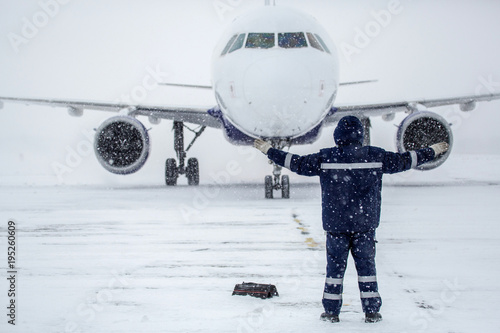 Member of ground crew park passenger airliner on airport apron in blizzard. passenger airliner taxi at airport in snow. Modern twin-engine passenger airplane taxiing at airport during snow blizzard