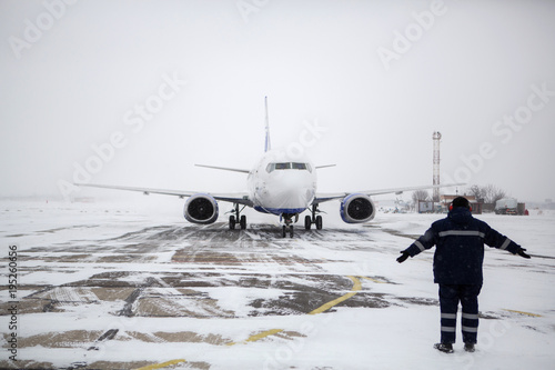 Fotografija Member of ground crew park passenger airliner on airport apron in blizzard