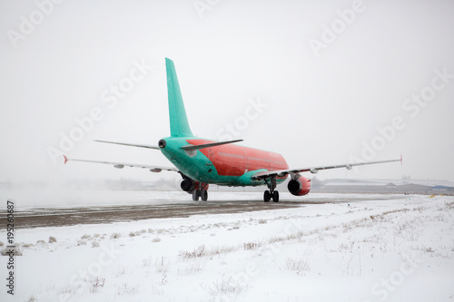 Fototapeta Naklejka Na Ścianę i Meble -  Airliner on runway in blizzard. Aircraft during taxiing at heavy snow. Passenger plane in snow at airport. Modern twin-engine passenger airplane taxiing for take off at airport during snow blizzard