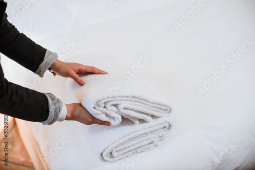 Female hands putting stack of fresh white bath towels on the bed