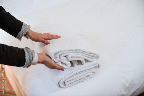Female hands putting stack of fresh white bath towels on the bed