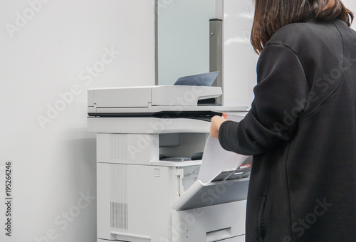 close up selective focus at businesswoman in black jacket put paper sheet into office printer tray for copying business documents
