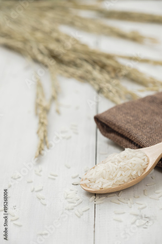 A wooden spoon filled with rice placed on wooden background.